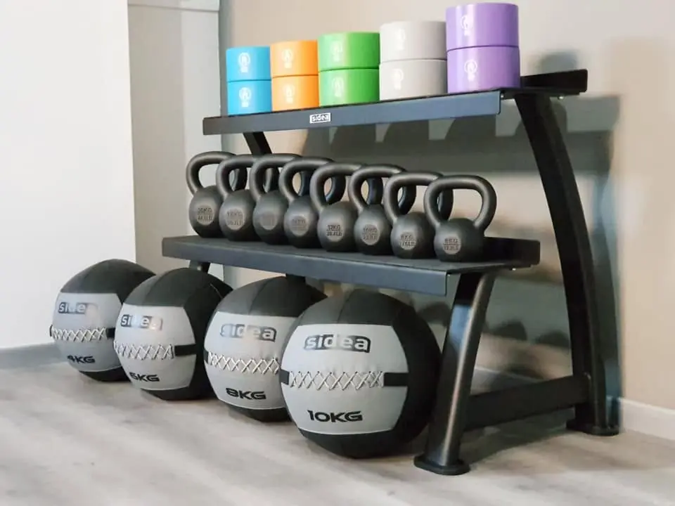 Kettlebell in fila, wall ball e rialzi colorati ordinati su una rastrelliera nella sala di My Personal Lab.